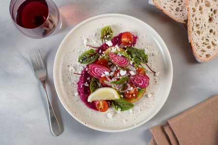 Gourmet avocado toast topped with candy‑striped beet slices, feta, tomatoes, and greens on a styled table, photographed in Newcastle.