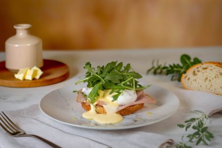 Eggs Benedict with ham, poached egg, hollandaise, and fresh Rocket on toast, photographed in a Newcastle kitchen setting.