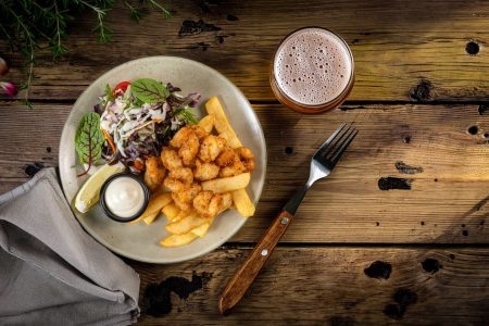 Plate of fried prawns with chips, coleslaw, lemon wedge, and beer on a rustic wooden table, photographed in Newcastle.