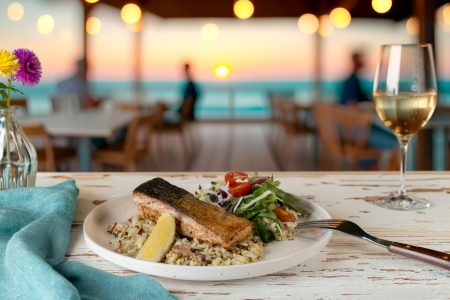 Grilled salmon served with rice, salad, and white wine at a seaside restaurant during sunset, photographed in Newcastle.