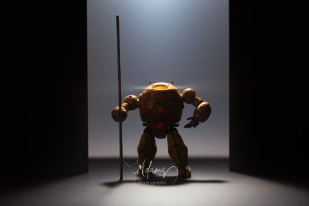 Miniature mech figure standing between dark panels with dramatic overhead lighting, photographed in Newcastle.